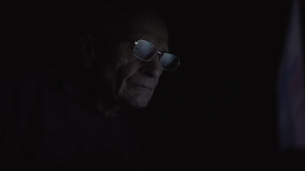 Senior volwassen werknemer in brillen werken op laptop monitor in donkere kamer — Stockvideo