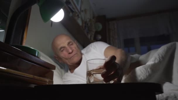 Κουρασμένος ηλικιωμένος άνδρας κάθεται στο κρεβάτι και έκανε μια γουλιά νερό από γυαλί — Αρχείο Βίντεο
