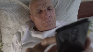 Yaşlı erkek geceleri uyanık ve telefon izliyor.