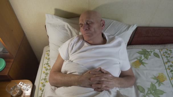 Άρρωστος παππούς ξαπλωμένος στο κρεβάτι του γηροκομείου και κοιμάται με ανησυχία ματιά — Αρχείο Βίντεο