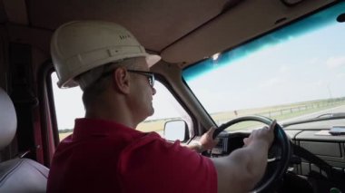 İnşaat kasklı ve güneş gözlüklü adam otoyolda hızla araba sürüyor.