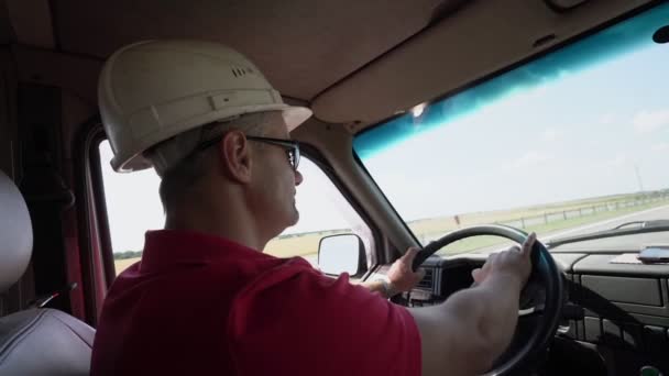 Человек в строительном шлеме и солнцезащитных очках быстро водит автомобиль по шоссе — стоковое видео