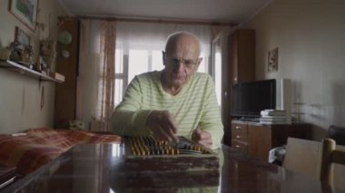 Evde gözlük takan olgun bir insan klasik abaküsle hesap yapıyor.