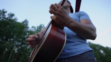 Güneş gözlüklü ve şapkalı erkek müzisyen parmaklarını oynatarak gitar çalıyor.