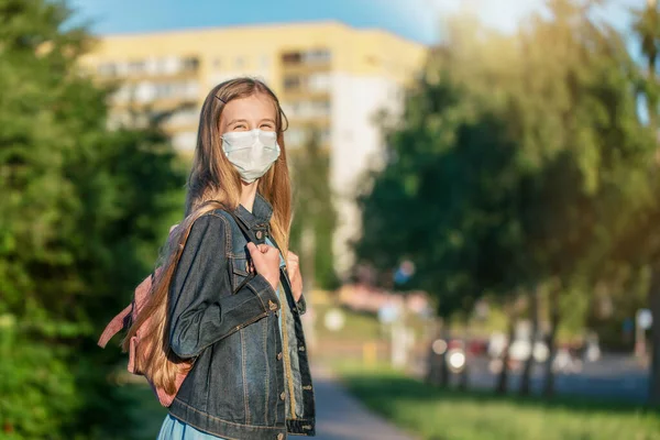 Школьница в медицинской маске стоит с рюкзаком на тротуаре — стоковое фото