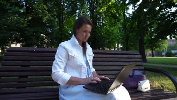 Самотня жінка працює на ноутбуці, дивлячись на екран в парку — стокове відео