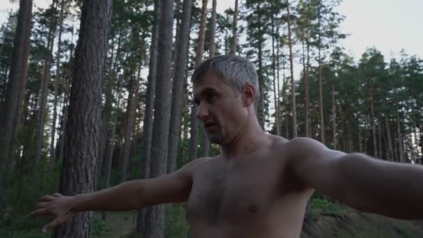Hombre hace ejercicios de respiración en el bosque concentrando y tensando su cuerpo — Vídeos de Stock