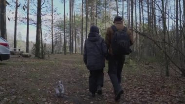 Yetişkin bir adam ve genç bir çocuk sonbahar ormanlarının arka penceresinde yürüyorlar.