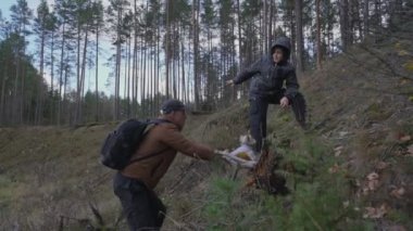 Sırt çantalı bir adam ve oğlu ve küçük şirin bir köpek orman dağına yükseliyor..