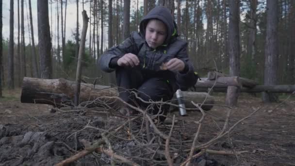 Один молодий хлопчик розпалює багаття з сухими гілочками і листям . — стокове відео