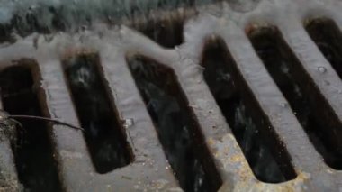 Eski paslı kanalizasyon ızgarasının ve şehir yolunda akan suyun yakın görüntüsü