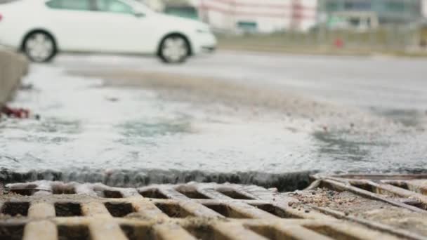 El agua derretida fluye hacia abajo en la carretera urbana con tráfico de vehículos — Vídeos de Stock