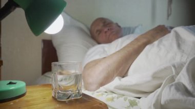 Yaşlı hasta büyükbaba beyaz battaniyeyle kaplı yatakta uyuyor.