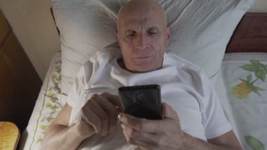 Yalnız büyükbaba yatakta uzanıyor ve akıllı telefon arıyor..