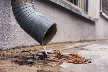 Atık su drenaj borusundan metal ızgaraya kuru yapraklarla akıyor.