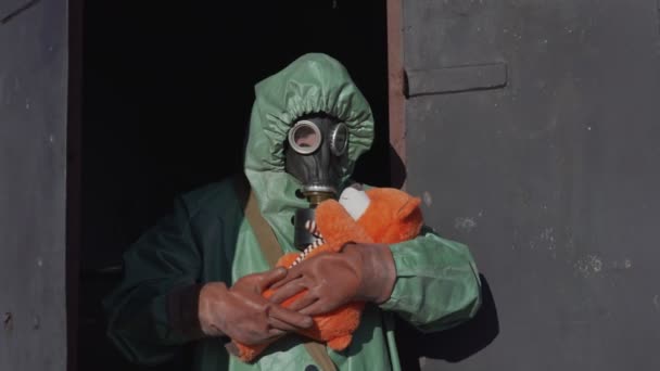 Hombre en capa protectora y máscara de gas columpios oso de peluche cerca de la puerta abierta — Vídeos de Stock