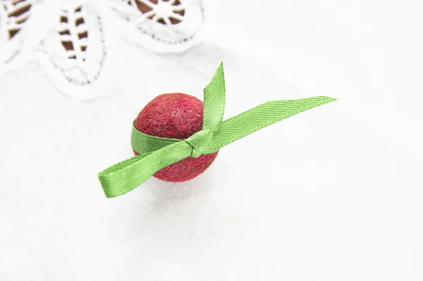 Red praline with green ribbon on white tablecloth — Stock Photo, Image