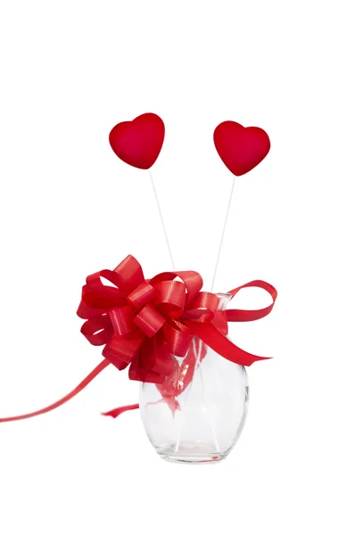 Стеклянная ваза с двумя красными сердцами и луком, белый фон — стоковое фото