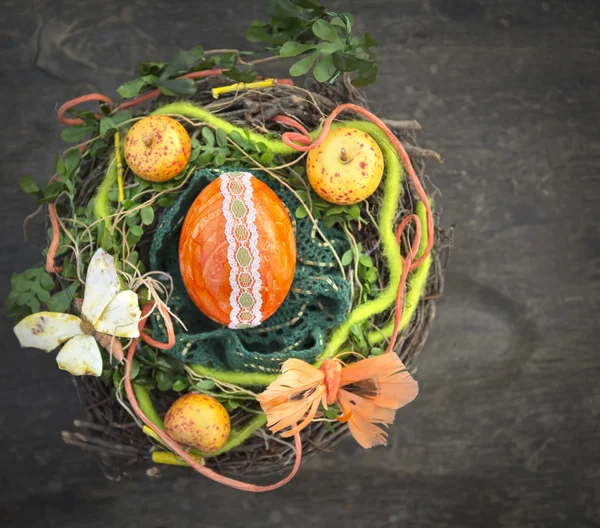 Orangefarbenes Osterei im Vogelnest mit Dekoration auf Holztisch — Stockfoto