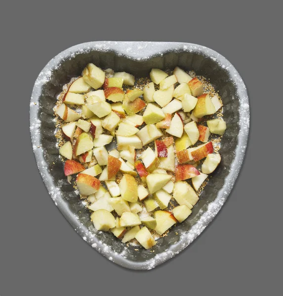 Pommes hachées au sucre et graines de sésame dans un plat allant au four En forme de coeur, isolées sur du gris — Photo