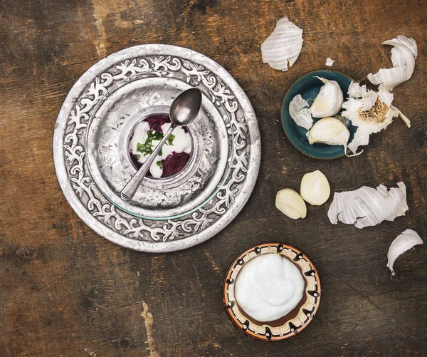 Варёная тертая свекла со сметаной и чесноком в стекле на серебряном блюдечке на старом деревянном столе — стоковое фото