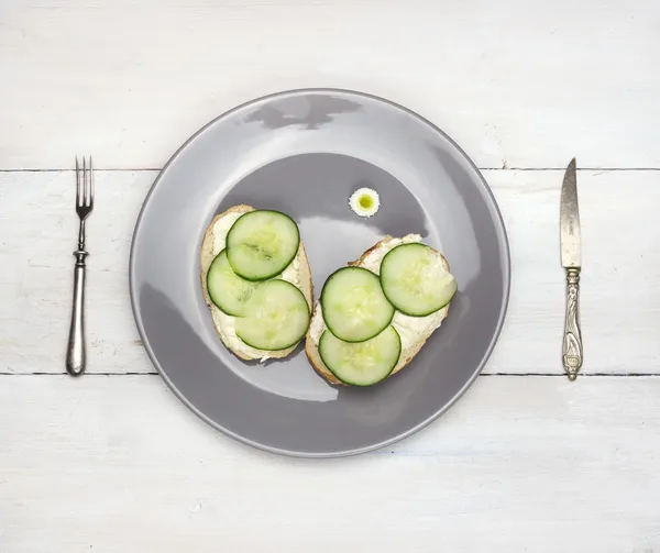 Sandwiches de pepino en plato gris con cuchillo y tenedor sobre mesa de madera blanca — Foto de Stock