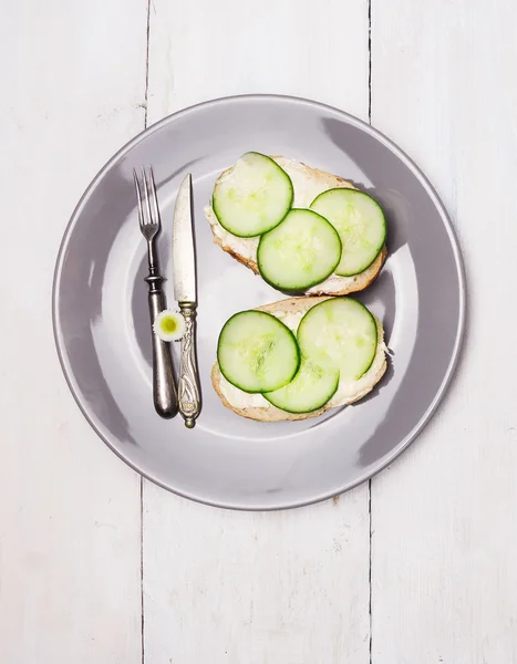Sandwiches de pepino Sirve en plato gris con cuchillo, tenedor y flor de margarita sobre fondo de madera blanca — Foto de Stock