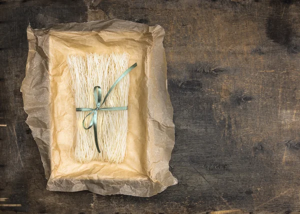Chinese rice noodles in crumpled paper packaging with green ribbon on an old wooden table