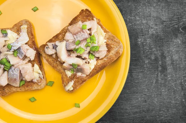 Salt herring sandwiches in the yellow plate on the old gray wooden table, close-up — Stock Photo, Image