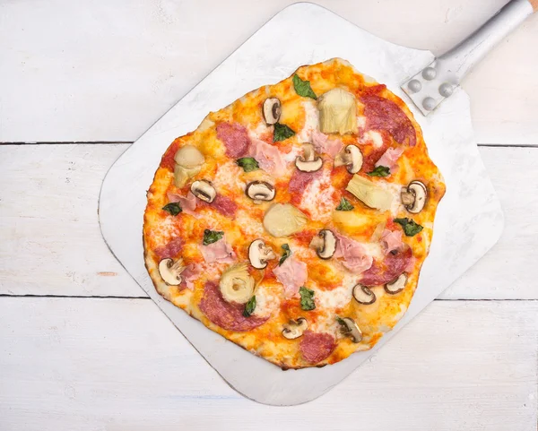 Pizza con salami, jamonera, alcachofa y champiñones sobre cáscara, mesa de madera blanca —  Fotos de Stock