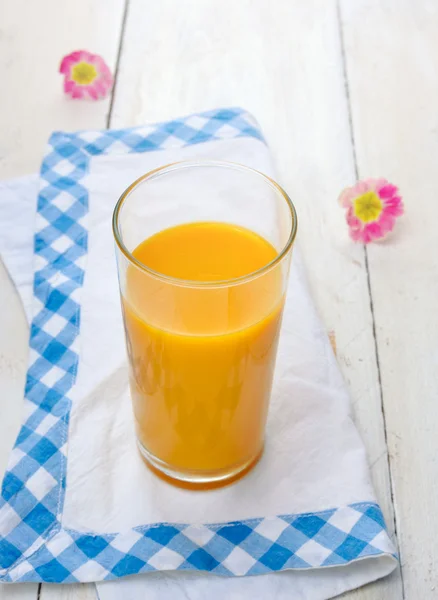 Vaso de la mañana de jugo amarillo sobre mesa blanca con tela azul y flores rosadas —  Fotos de Stock