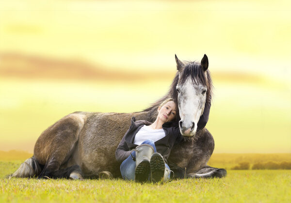 Pretty girl and gray Arabian horse lie at sunset on  summer pasture