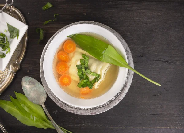 Soup with ravioli,carrots and ramson leafs in silver plate with vintage spoon — Stock Photo, Image