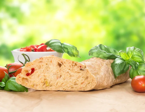 Italian bread  ciabatta with tomatoes and basil on table in green garden — Stock Photo, Image