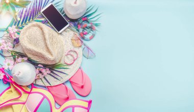 Yaz plajı aksesuarları. Kız takımı. Hasır şapka, bikini, terlik, güneş gözlüğü ve arka planda palmiye yaprakları ve hindistan cevizi içecekleri olan akıllı telefon. Tropik tatil