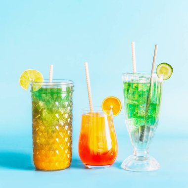 Renkli yaz mevsimleri ferahlatıcı limonata uzun içecekler buz küpleri ve bardaklarda kokteyller kağıt kamışlarla içme ve mavi arka planda narenciye meyveleri.