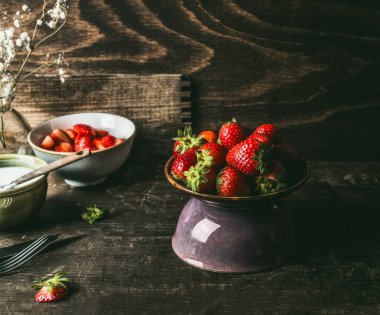 Koyu kırsal mutfak arka planında çilek kasesiyle hayat devam ediyor