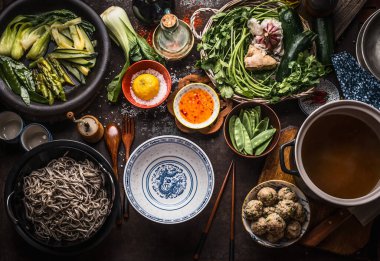 Asian noodle soup ingredients: various fresh and cooked green vegetables, herbs and spices , meat balls , soba noodle and chopsticks around empty asian bowl, top view. Copy space. Asian ingredients