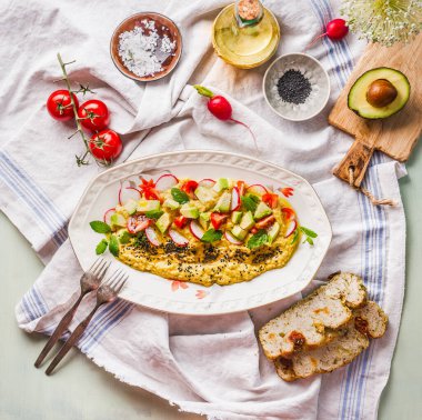Delicious hummus plate topped with olive oil, avocado, fresh vegetables and herbs served on kitchen table with fork and bread, top view. Vegan food concept. Healthy snack. Mediterranean lunch.