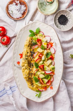 Homemade hummus plate topped with olive oil, avocado, fresh vegetables and herbs  on kitchen table, top view. Vegan food concept. Healthy food. Mediterranean lunch.