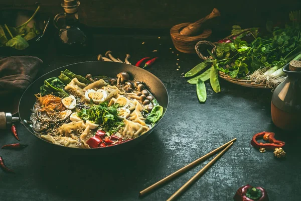 Asian food background with wok pan with vegetarian  korean hot pot and chopsticks on dark rustic kitchen table background, top view. Copy space.