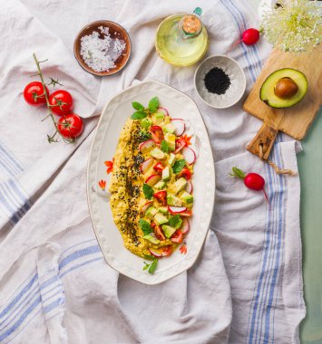 Tasty hummus plate topped with  avocado and fresh sliced vegetables and herbs  on kitchen table with ingredients, top view. Vegan food concept. Healthy snack.