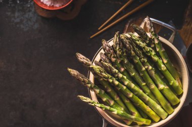 Fresh green asparagus in asian bamboo steamer on dark background, top view. Copy space. Healthy eating and cooking concept. Diet food