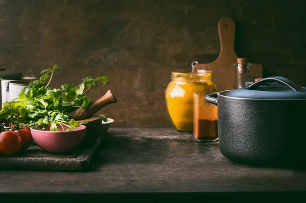 Food background with cast iron cooking pot, fresh seasoning and spices on rustic kitchen table. Copy space. Healthy eating, clean food concept