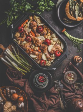 İçinde çeşitli malzemeler, çatallar ve mutfak ekipmanları olan fırında taze pişmiş yemekler koyu beton arka planda mutfak bezi, düz bir zemin. Üst görünüm