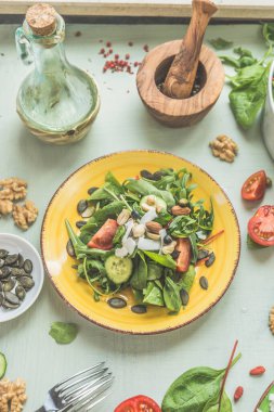 Sarı tabakta fındıklı sağlıklı yeşil vejetaryen salatası. Vejetaryen salata sosu ve malzemeler. Üst Manzara. Vejetaryen yemeği.