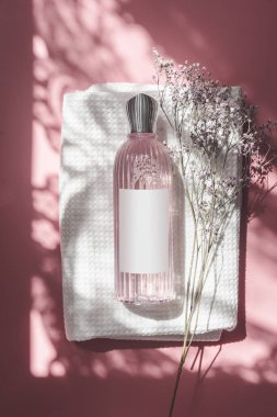 Pembe kozmetik şişesi. Beyaz havluyla etiketlenmiş. Pembe arka planda. Üst görünüm