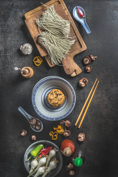 アジアの食材 自家製のまな板麺 アジア料理の伝統的なボウル チリペッパー ソース瓶 暗い素朴な背景の箸がたくさんあります トップ表示 ロイヤリティフリーのストック画像