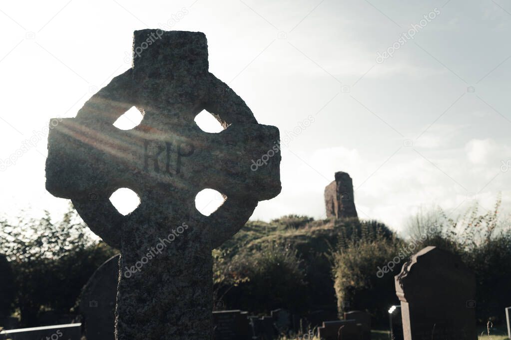 A spooky concept of a cross in a graveyard. Backlighted by the setting sun.