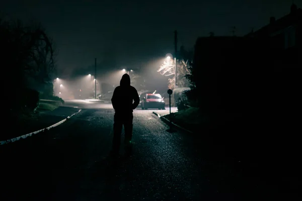 怖いフードのフィギュアのムーディーなコンセプト 静かな郊外の通りでは 道路の真ん中に立っている 霧の多い冬の夜に — ストック写真